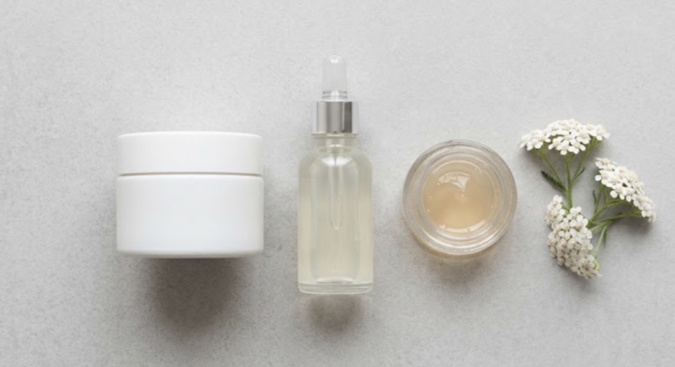 Krem kavanozu, serum şişesi ve jel kabı ile civanperçemi çiçekleri